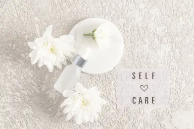 Selfcare routine tijdens de overgang. Bord met witte bloemen en een flesje parfum.